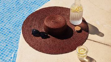 Escena junto a la piscina con un sombrero de paja tejido, gafas de sol, una botella de vidrio con una rodaja de limón y un corcho.