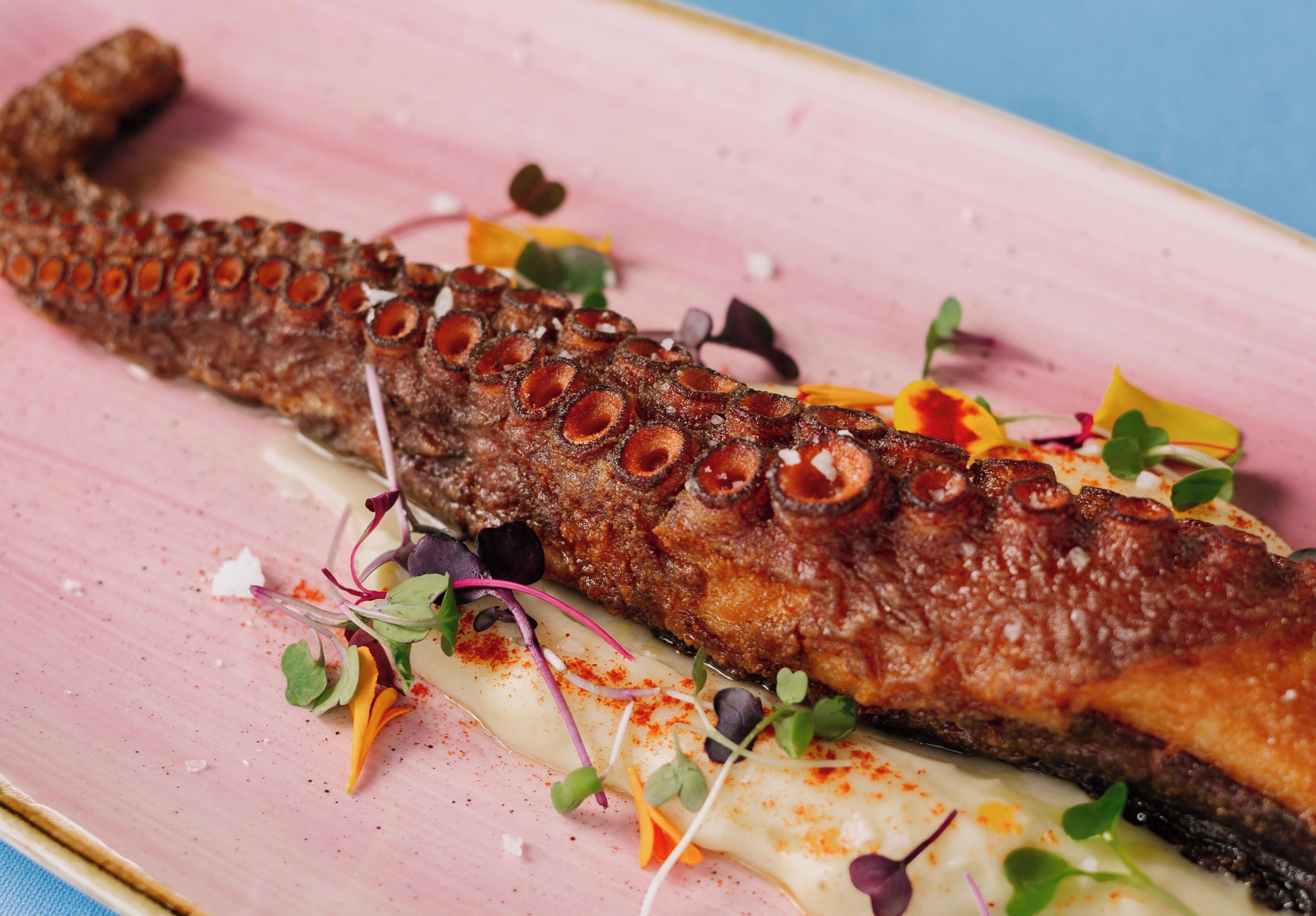 A dish with a whole fish, garnished with greens and spices, on a pink plate.