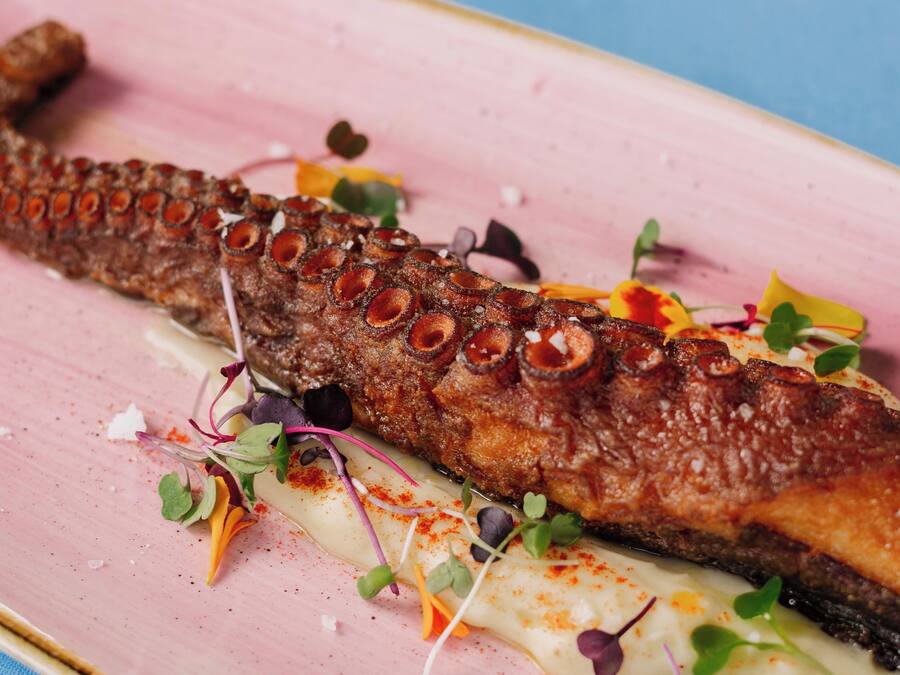 A dish with a whole fish, garnished with greens and spices, on a pink plate.