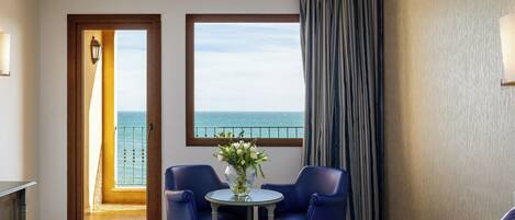 A hotel room with a balcony, two blue chairs, a small table with a vase, and a bed.