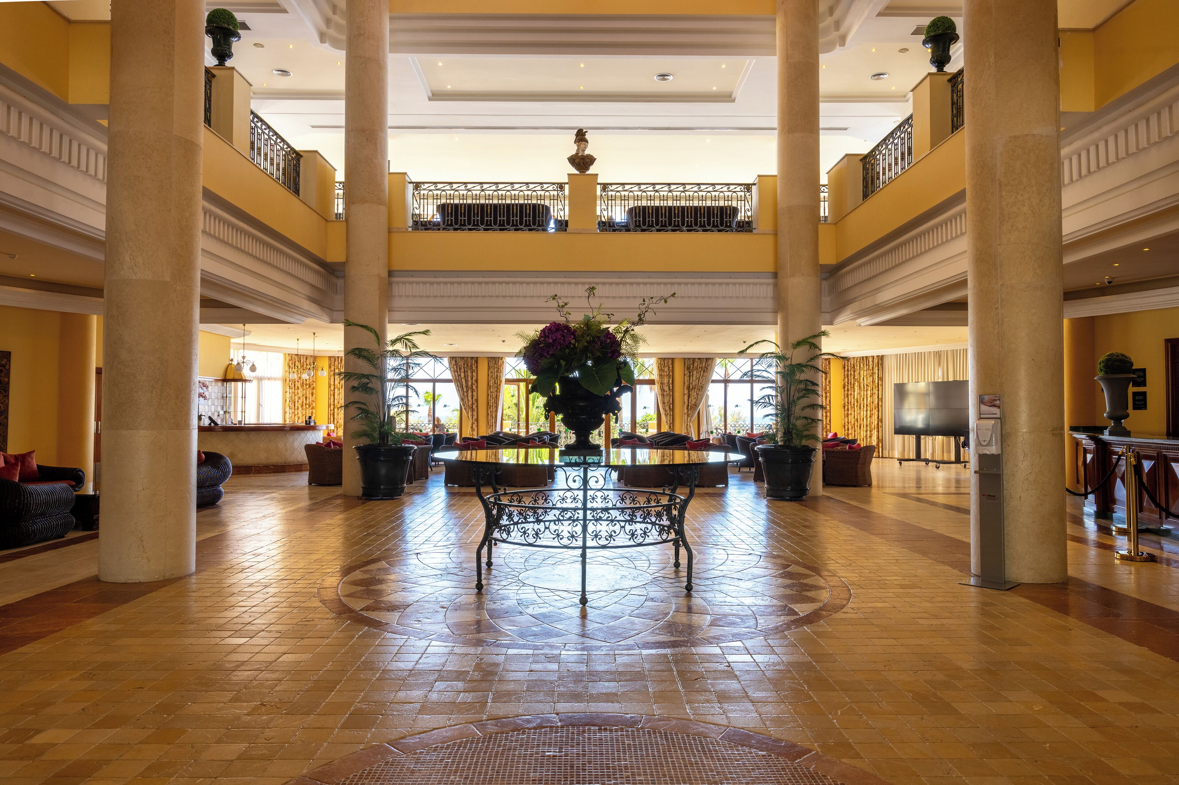 A spacious lobby with a central table, multiple seating areas, and a high ceiling with decorative elements.