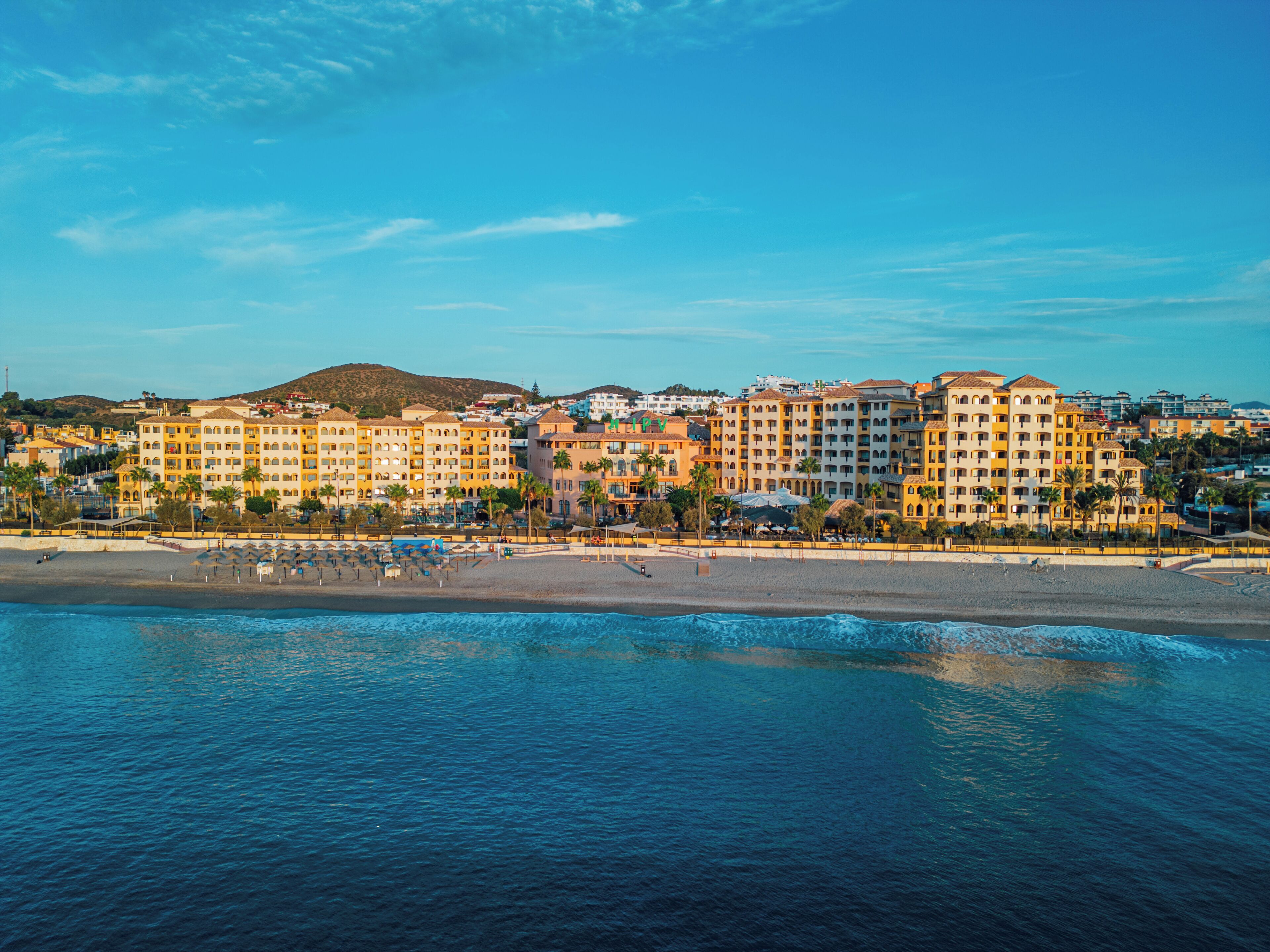 Un hotel frente al mar con varias edificaciones, una playa y vistas al océano.