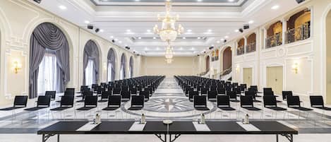 A large conference room with rows of black chairs, a central table, and a chandelier.