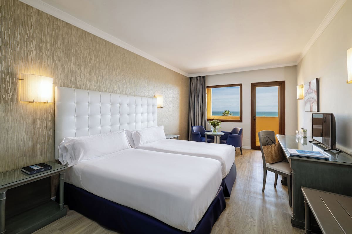 Een hotelkamer met twee bedden, een bureau, een stoel, een televisie en uitzicht op de oceaan.