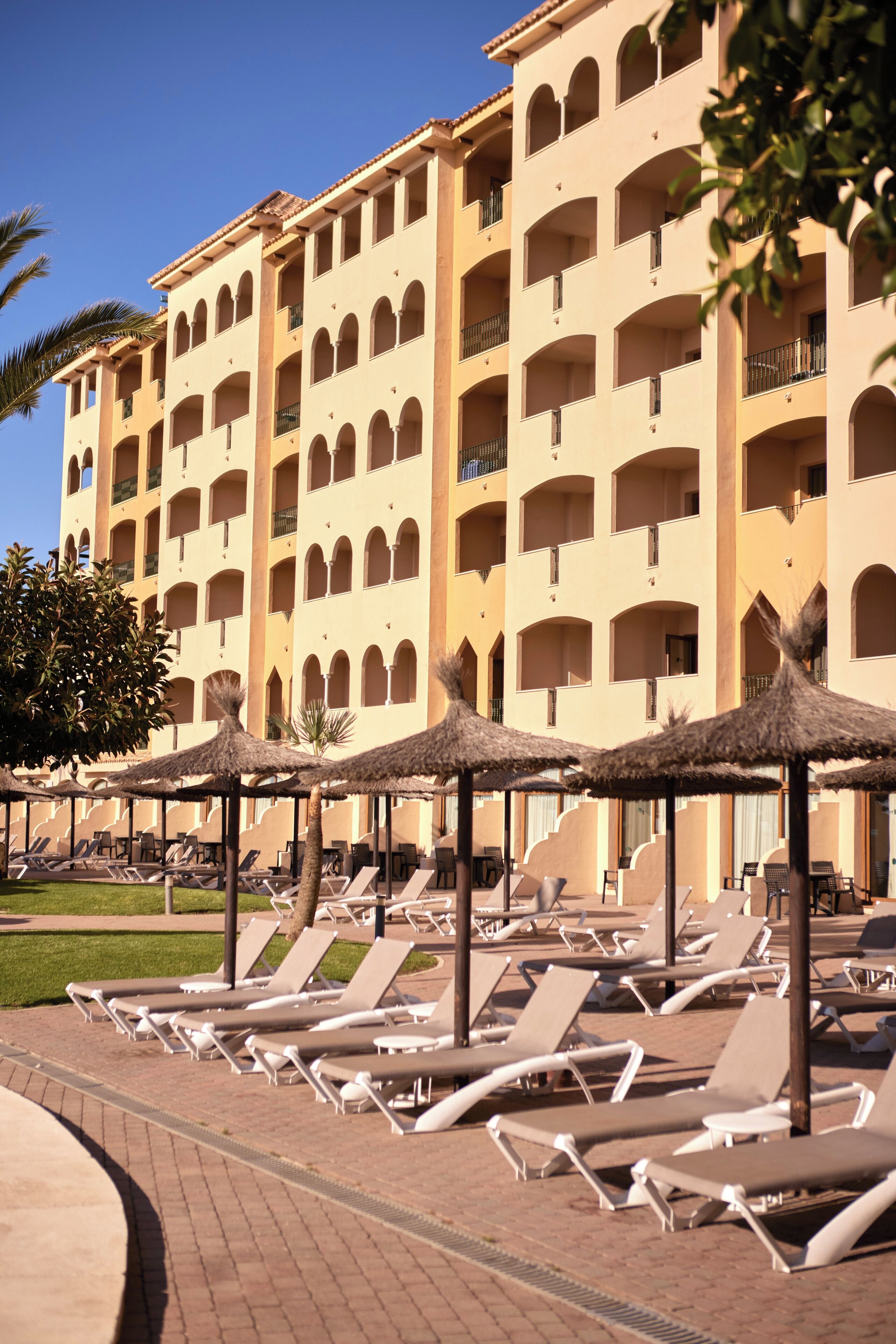 Un hôtel doté de nombreux balcons, de chaises longues et de parasols en chaume.