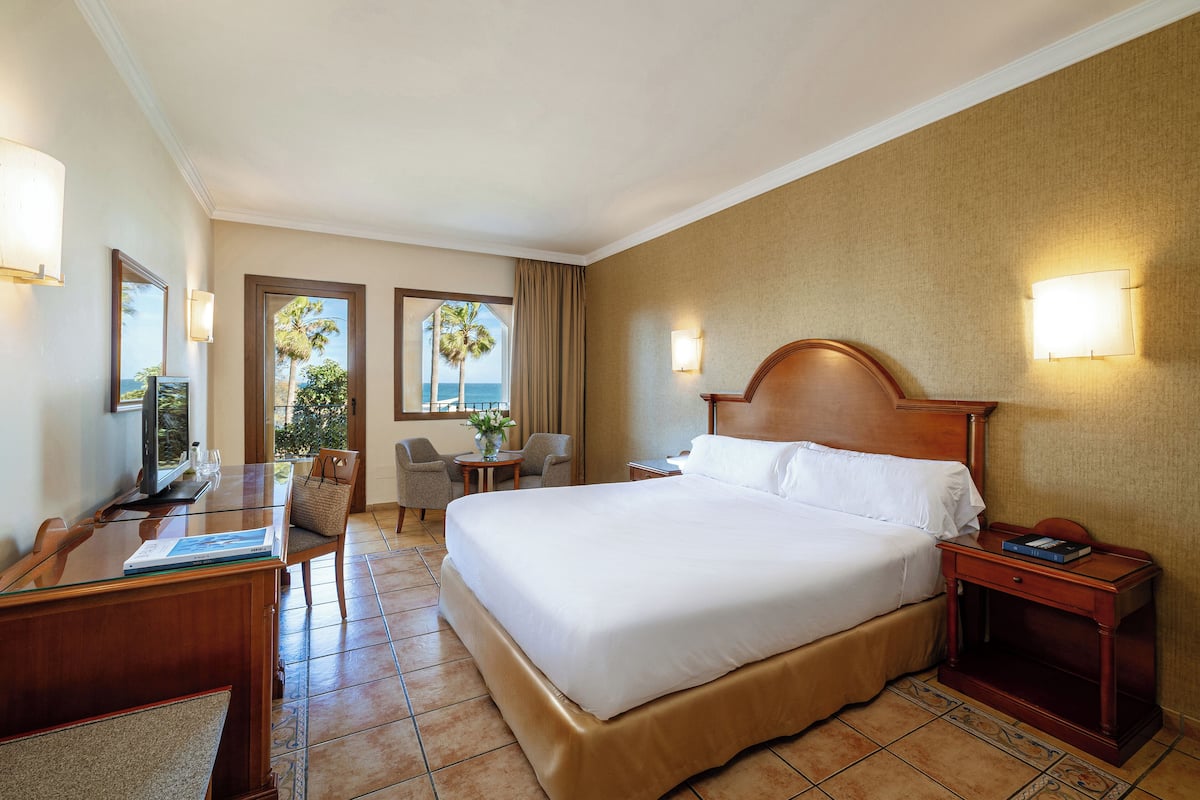 Een hotelkamer met een groot bed, een bureau met stoel, een klein tafeltje en een nachtkastje.