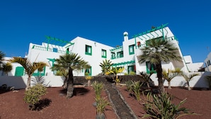 A white building with green accents, surrounded by palm trees and a stone pathway. - BLUESEA Los Fiscos (Tías)