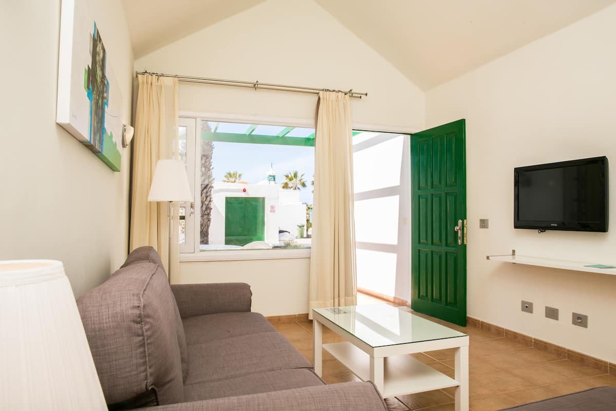 Een woonkamer met een bank, een glazen tafel, een aan de muur bevestigde televisie en een groene deur.