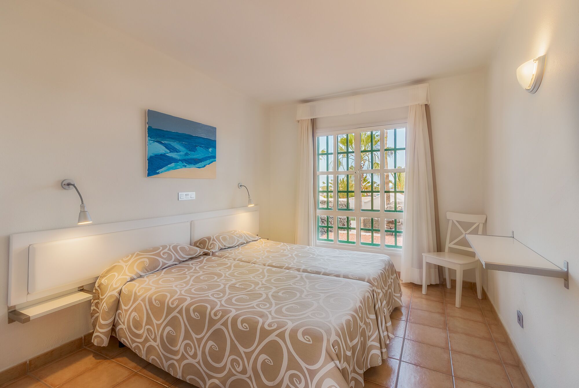 Un dormitorio con dos camas, un escritorio, una silla, una ventana con cortinas y un cuadro colgado en la pared.