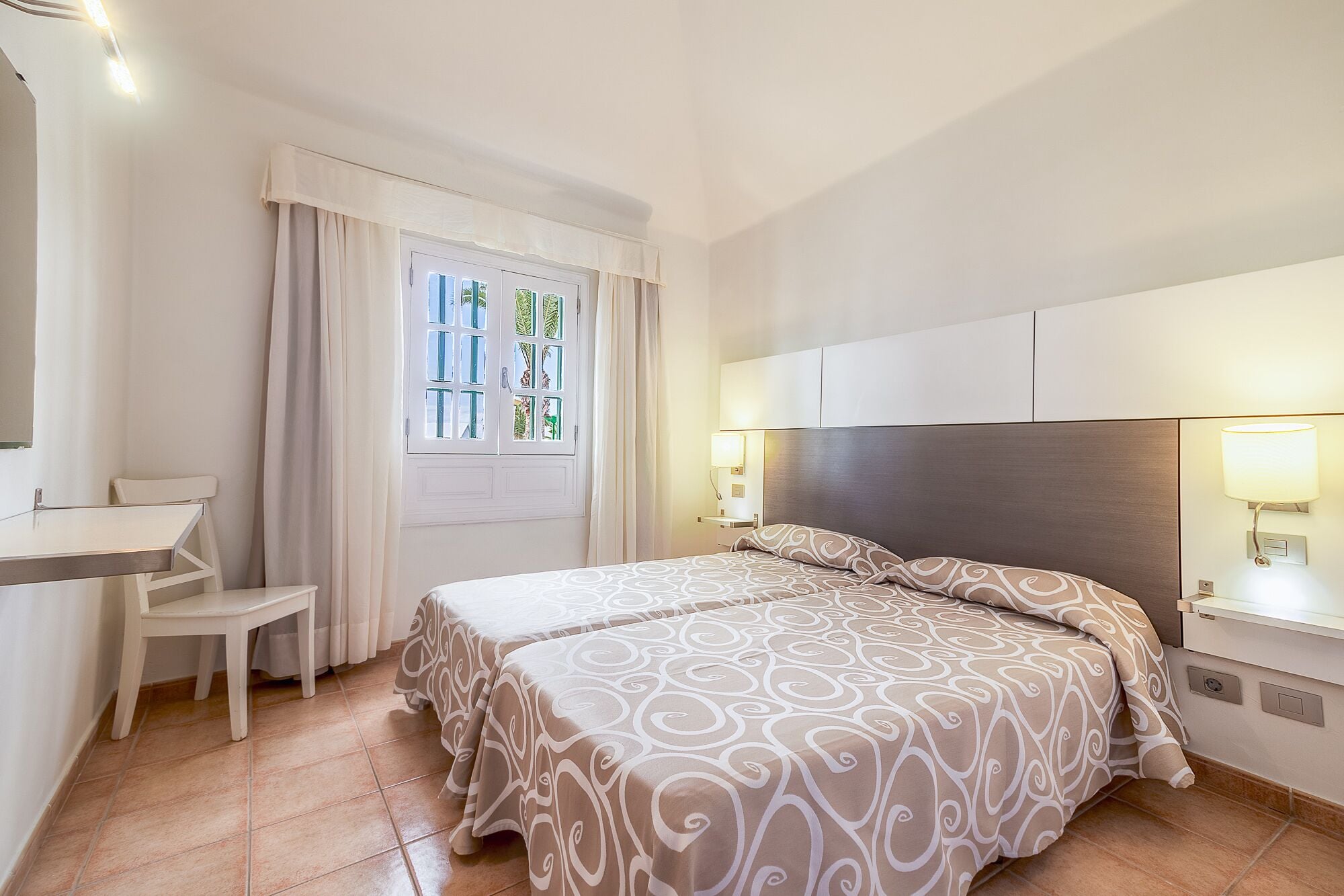 Ein Hotelzimmer mit Bett, Schreibtisch und einem Vorhangfenster.