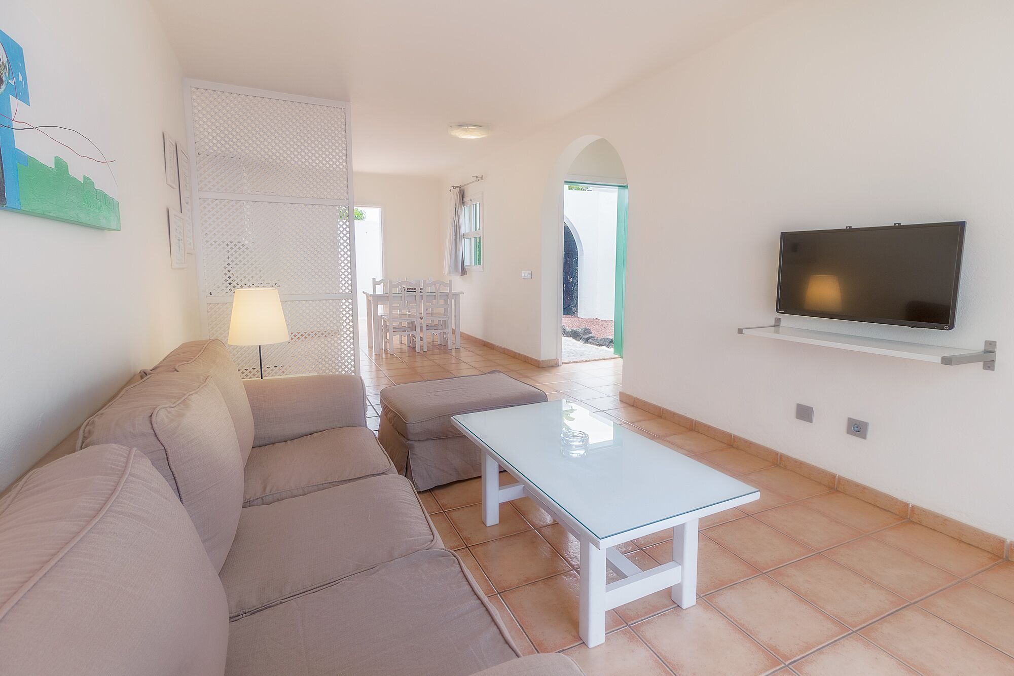 Una sala de estar moderna con un sofá, una mesa de centro de vidrio y un televisor montado en la pared.