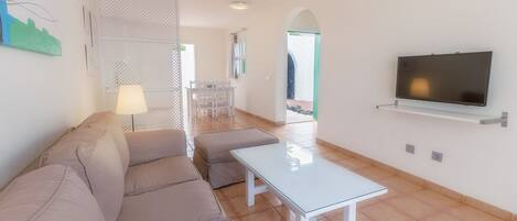 Una sala de estar moderna con un sofá, una mesa de centro de vidrio y un televisor montado en la pared.