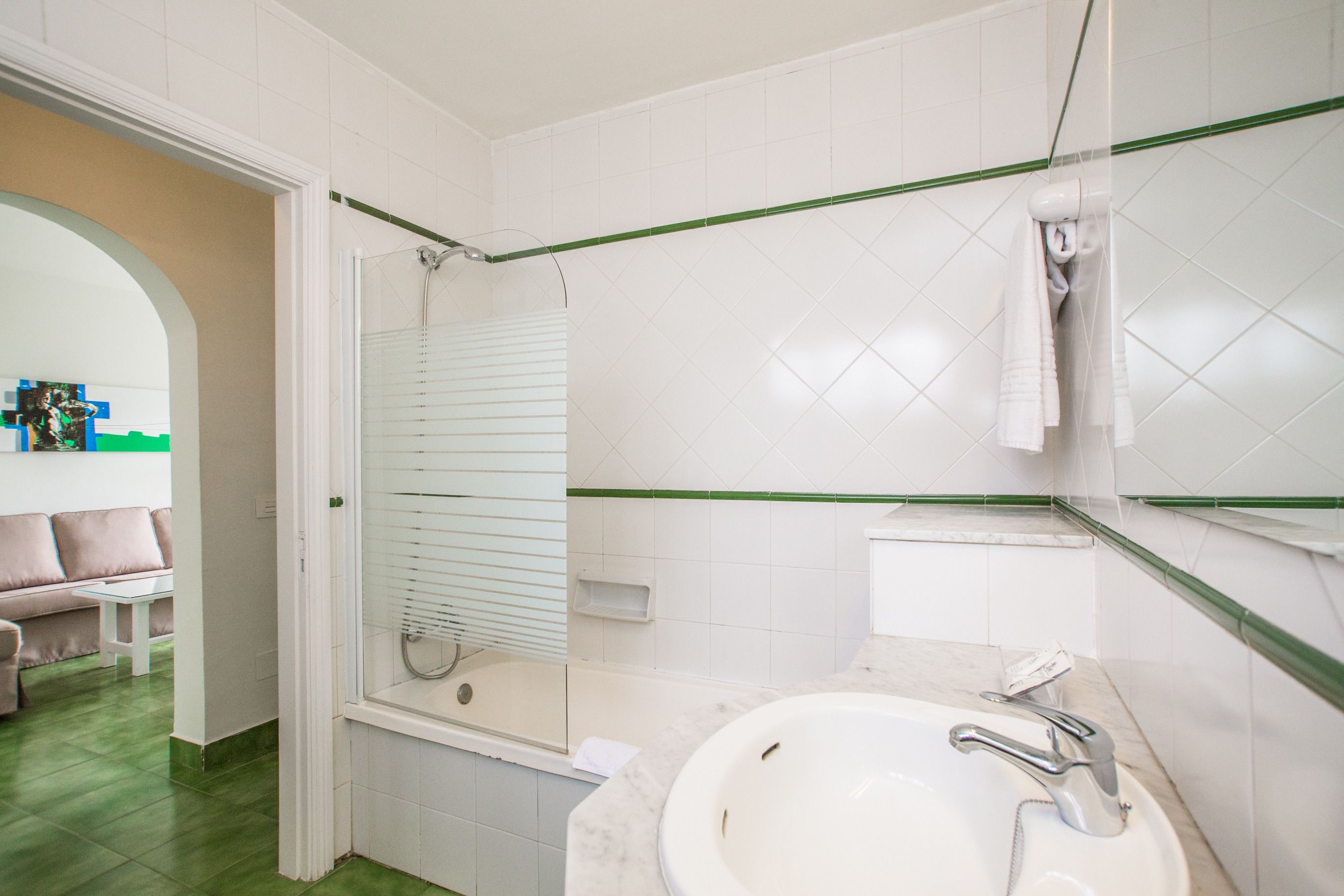 Un baño con un lavamanos blanco, una cabina de ducha con mampara de vidrio y un espejo con una toalla colgada.