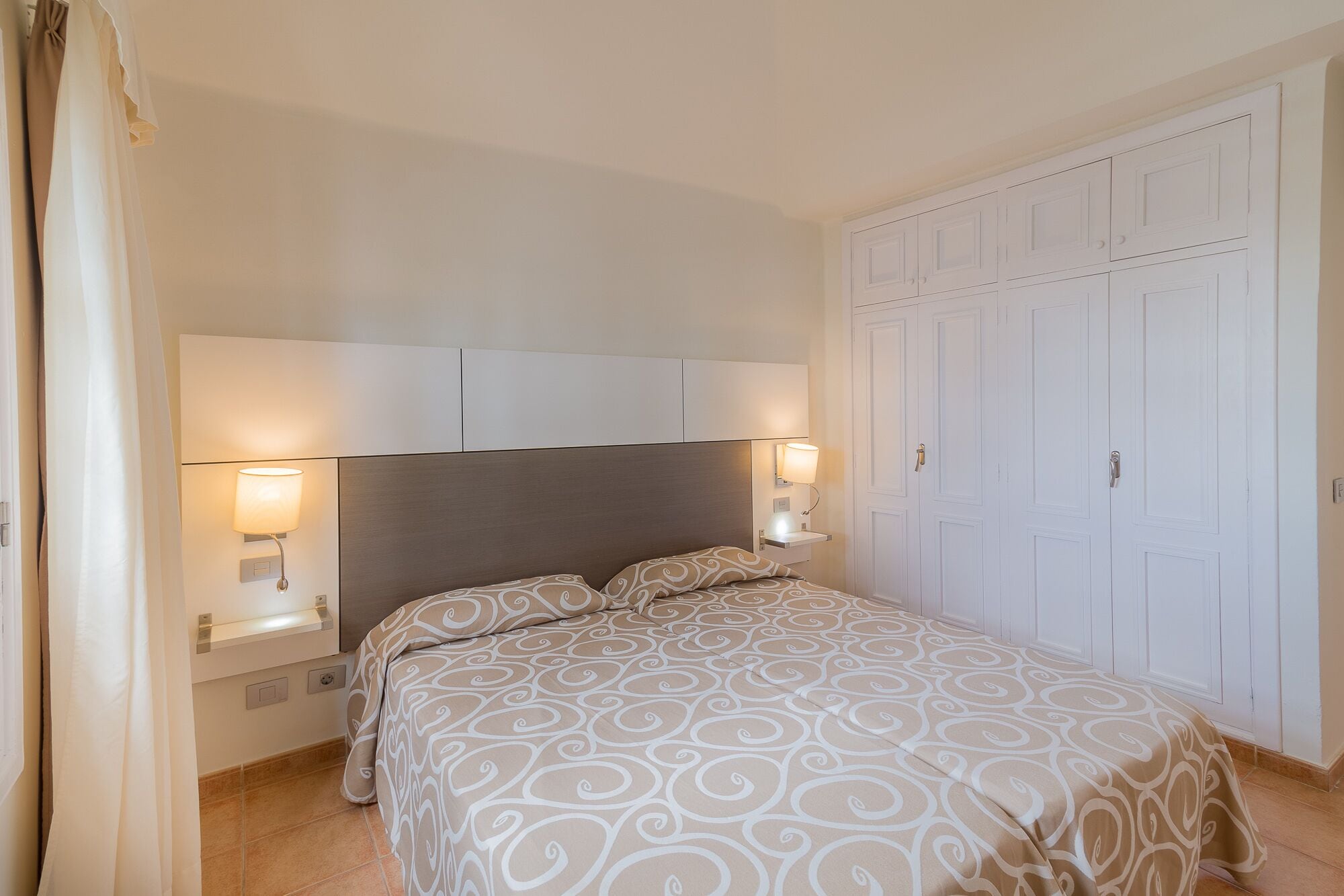 A bedroom with a bed, two bedside lamps, a nightstand, and a wardrobe.