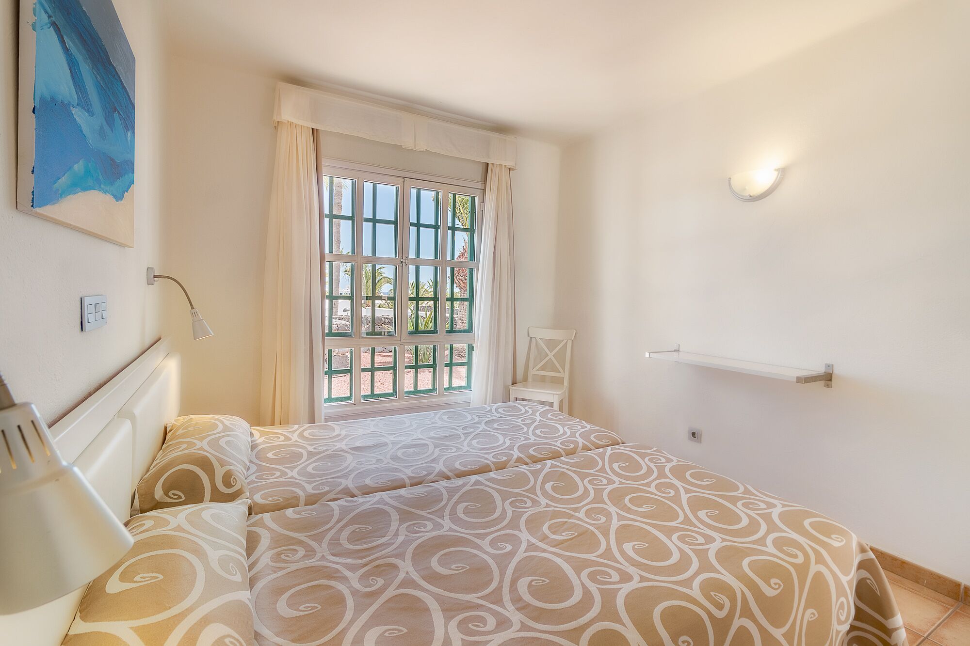 Un dormitorio con una cama, una ventana con cortinas, una silla y un estante fijado a la pared.