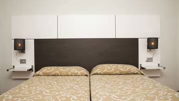 Un lit double avec une couvre-lit à motifs, une tête de lit sombre et deux tables de chevet fixées au mur, chacune équipée d’une lampe.