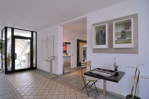 A modern hotel lobby with a tiled floor, a reception desk, and framed pictures on the wall.