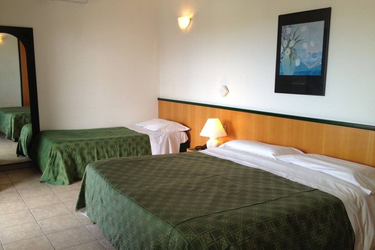 A hotel room with two single beds, a nightstand with a lamp, a painting on the wall, and a mirror on the door.