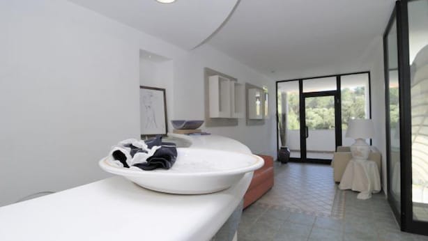 A modern bathroom with a large white sink, a mirror, and a window providing natural light.