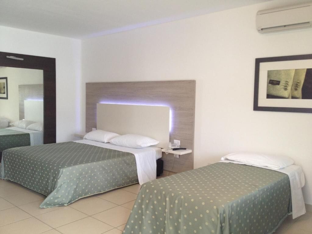 A hotel room with two beds, a bedside table, a mirror, and a wall-mounted air conditioner.