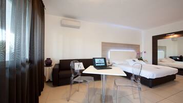 A hotel room with a bed, a desk with a laptop, a chair, a sofa, and a large mirror.
