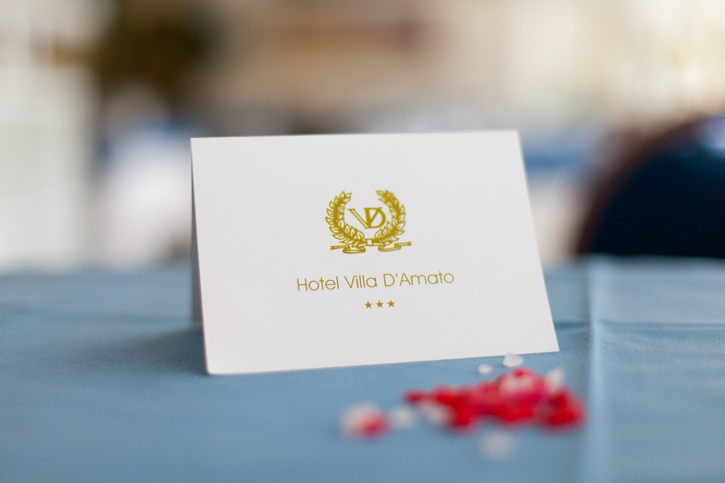 A white business card with the text "Hotel Villa D'Amato" and a gold emblem.