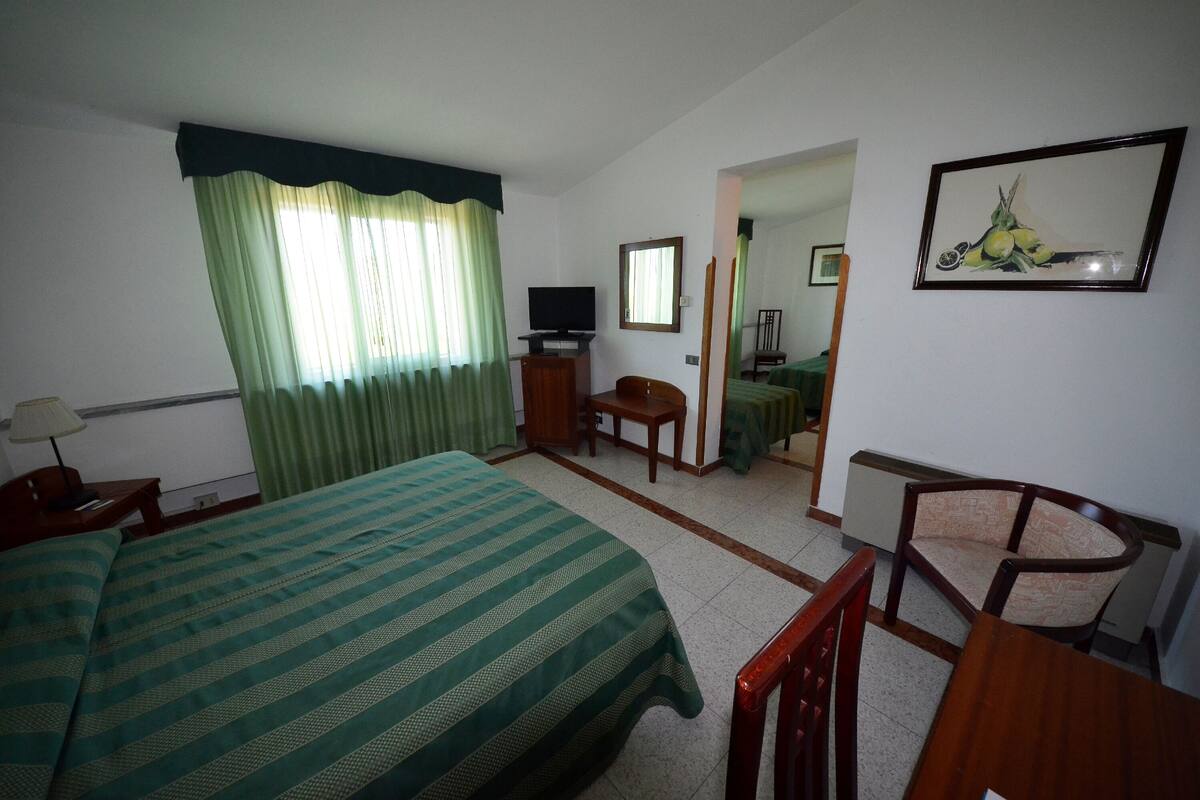 A hotel room with a bed, a desk, a chair, a television, and a painting on the wall.