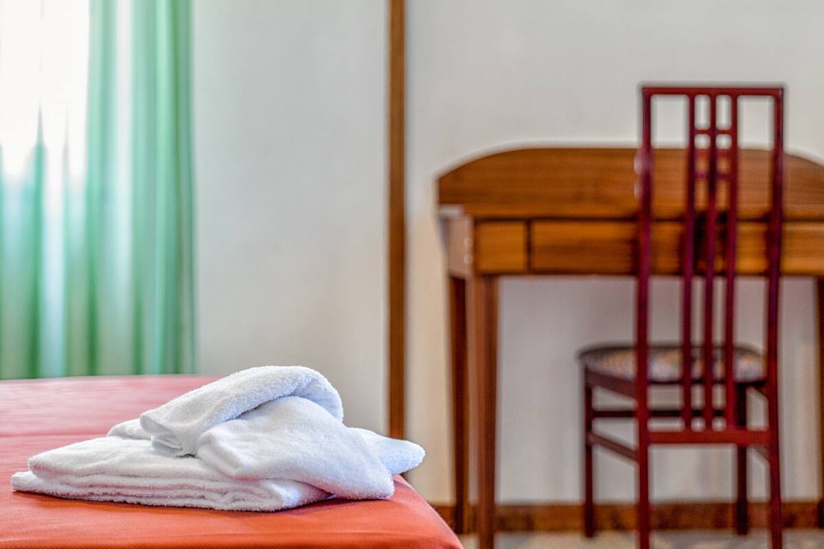 A neatly made bed with a red bedspread and a stack of white towels on top.