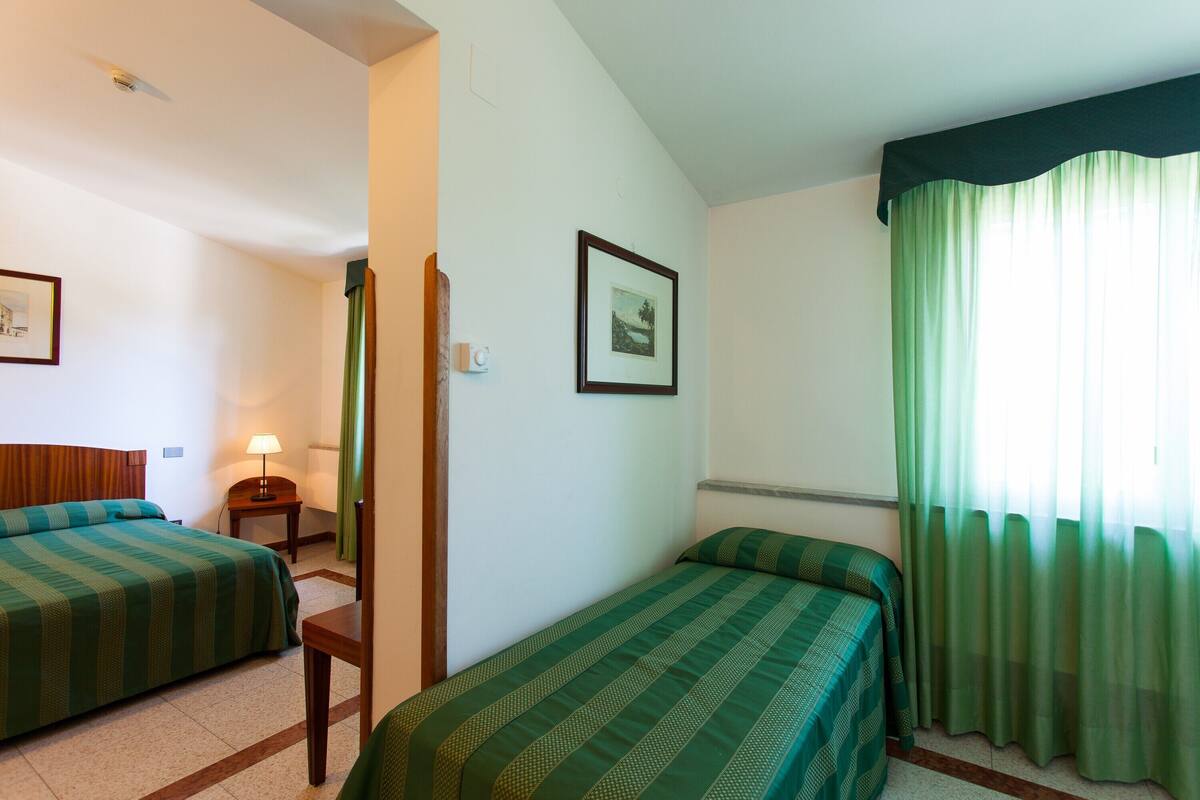 A hotel room with two beds, a nightstand, a lamp, and a framed picture on the wall.