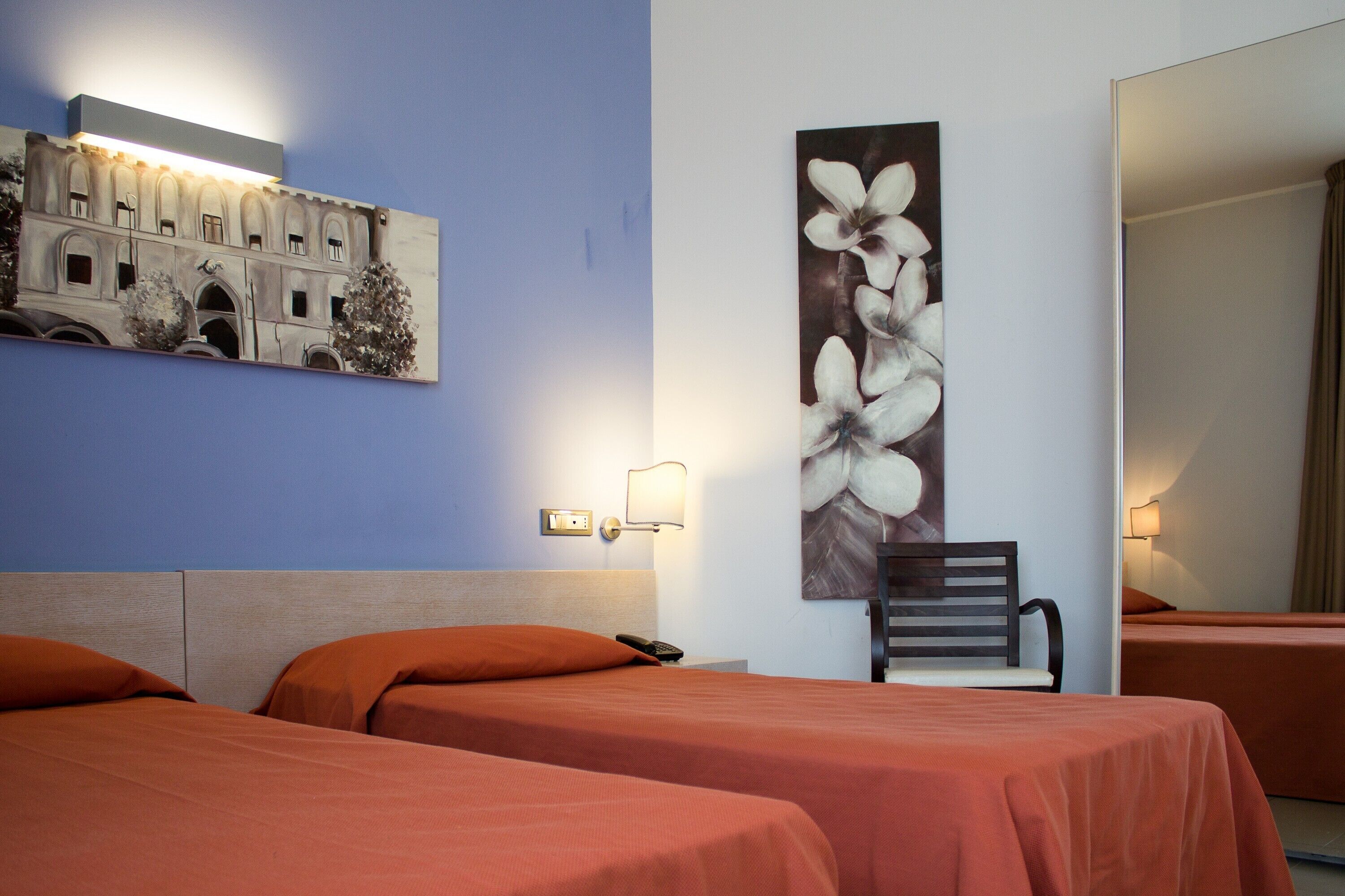 Una camera d'albergo con due letti, un comodino, una lampada e un quadro appeso al muro.