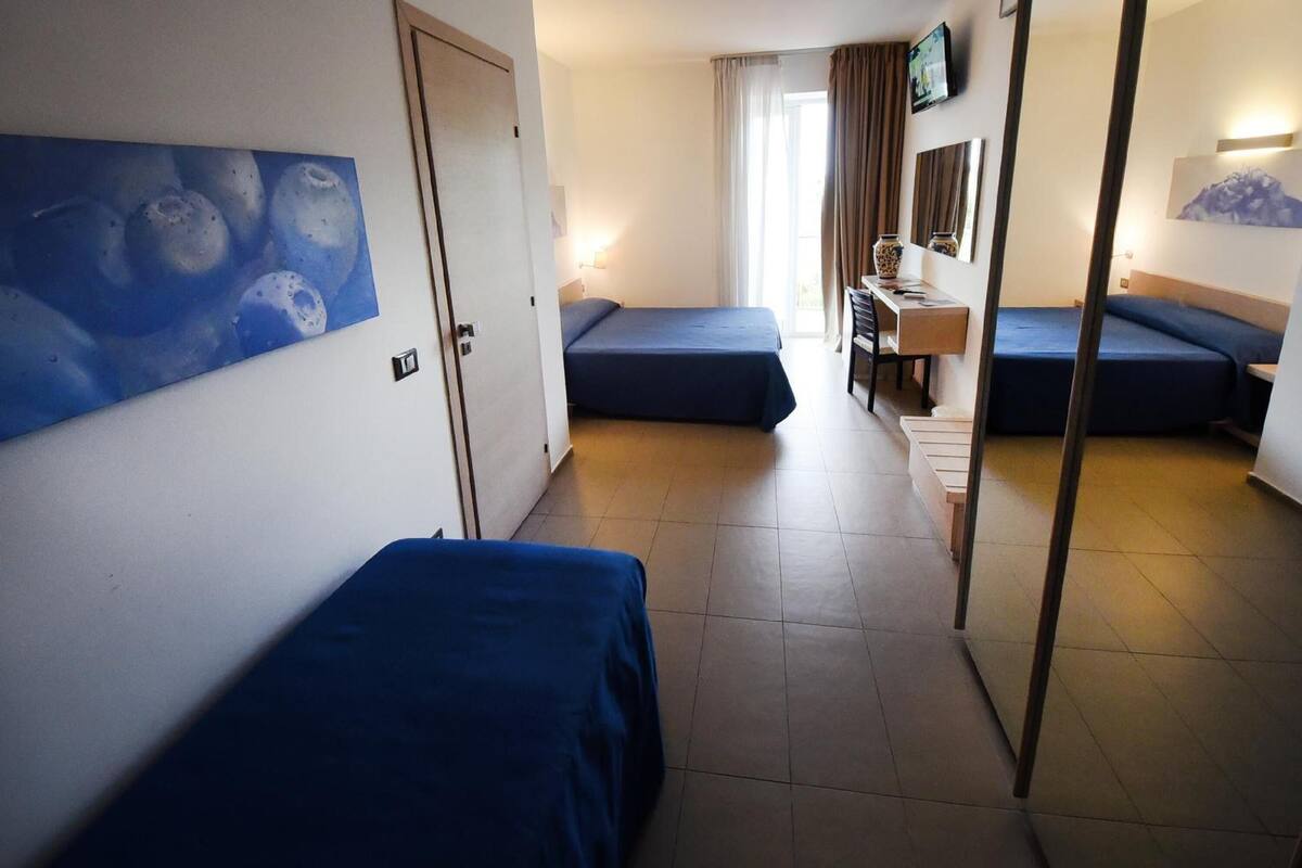 A hotel room with two beds, a desk, a chair, a television, and a painting on the wall.