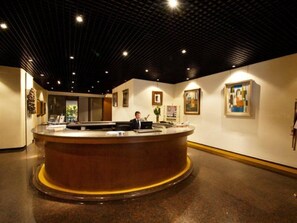 Een receptiegedeelte met een rond aanrecht, een receptie medewerker en ingelijste kunstwerken aan de muren.