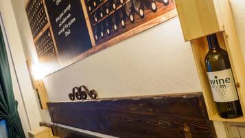 Une tête de lit en bois sur laquelle est posée une bouteille de vin, une étagère, un mur avec un porte-bouteilles et un lit recouvert d’une couvre-lit à motifs.