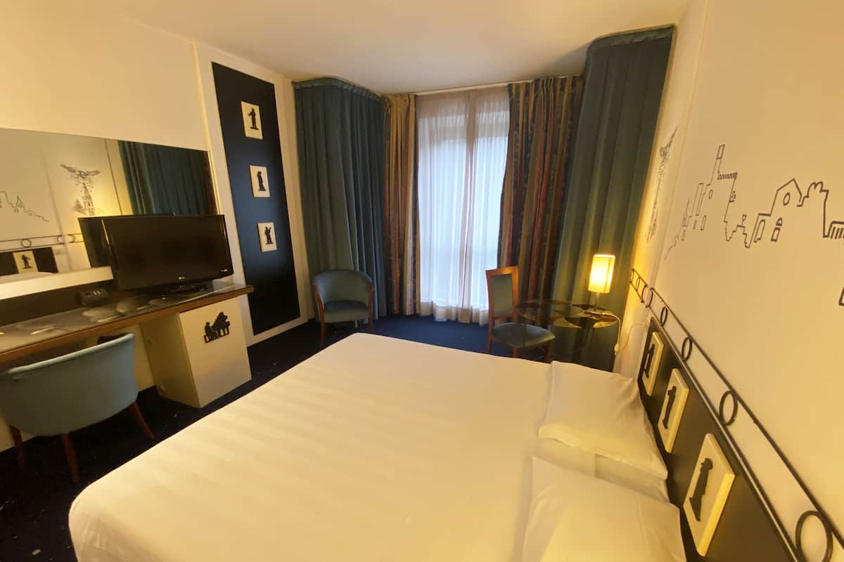 A hotel room with a bed, desk, television, and seating area.