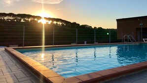 Piscina com um pôr do sol ao fundo, cercada por uma grade e um edifício.