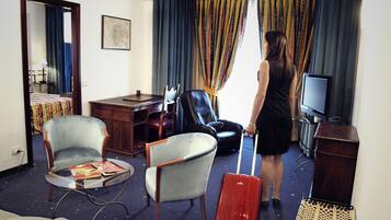 A hotel room with a bed, a desk, a television, a chair, a suitcase, and a window with curtains.