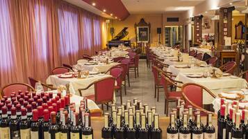 Un restaurant avec de nombreuses tables dressées pour le service, un piano en arrière-plan et de nombreuses bouteilles de vin exposées au premier plan.