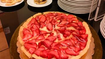 A round dessert with sliced strawberries on top, surrounded by plates and bowls.