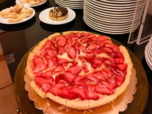 Un postre redondo con fresas en rodajas encima, rodeado de platos y tazones.