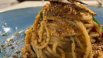 Un plato de espagueti con cobertura crujiente y un trozo de pescado encima.