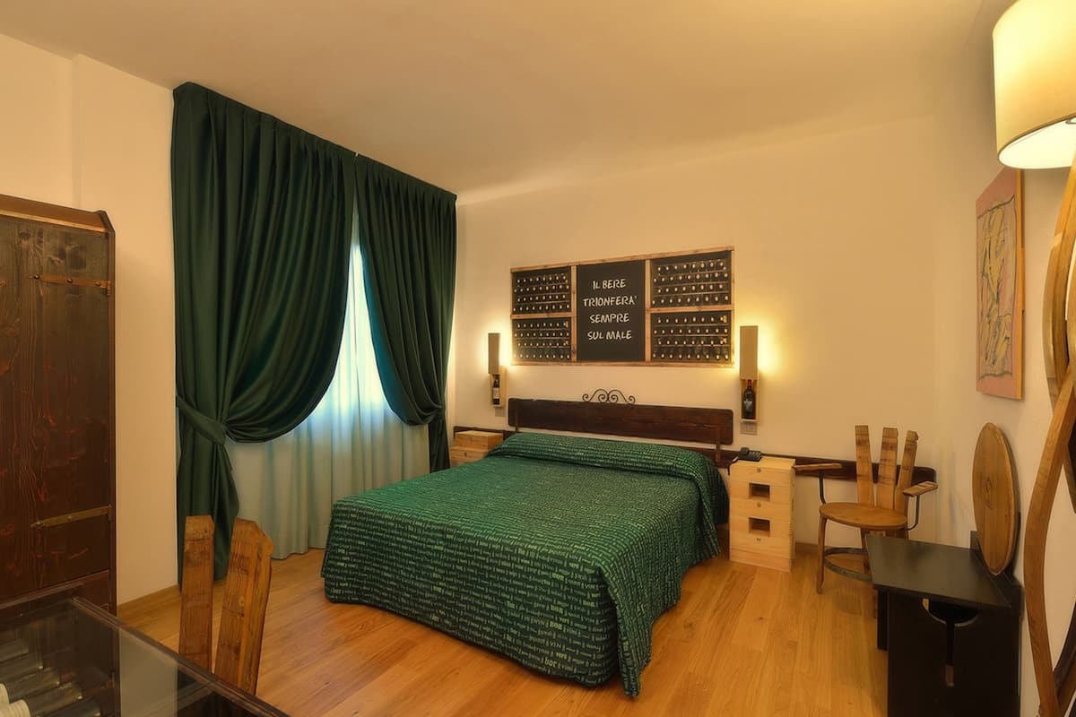 A hotel room with a wooden bed, a desk, a chair, and a wall-mounted wine rack.