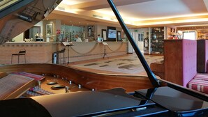 Um piano de cauda num hall amplo, com um balcão de recepção, área de bar e vista para o interior.