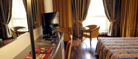 Una habitación de hotel con una cama, un escritorio con televisor, una silla y una lámpara.