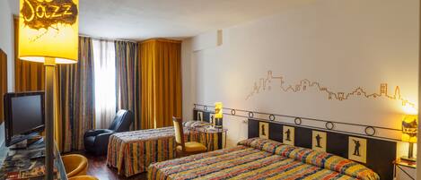 Quarto de hotel com duas camas, uma escrivaninha com computador, uma cadeira e um abajur identificado como 'Jazz'.
