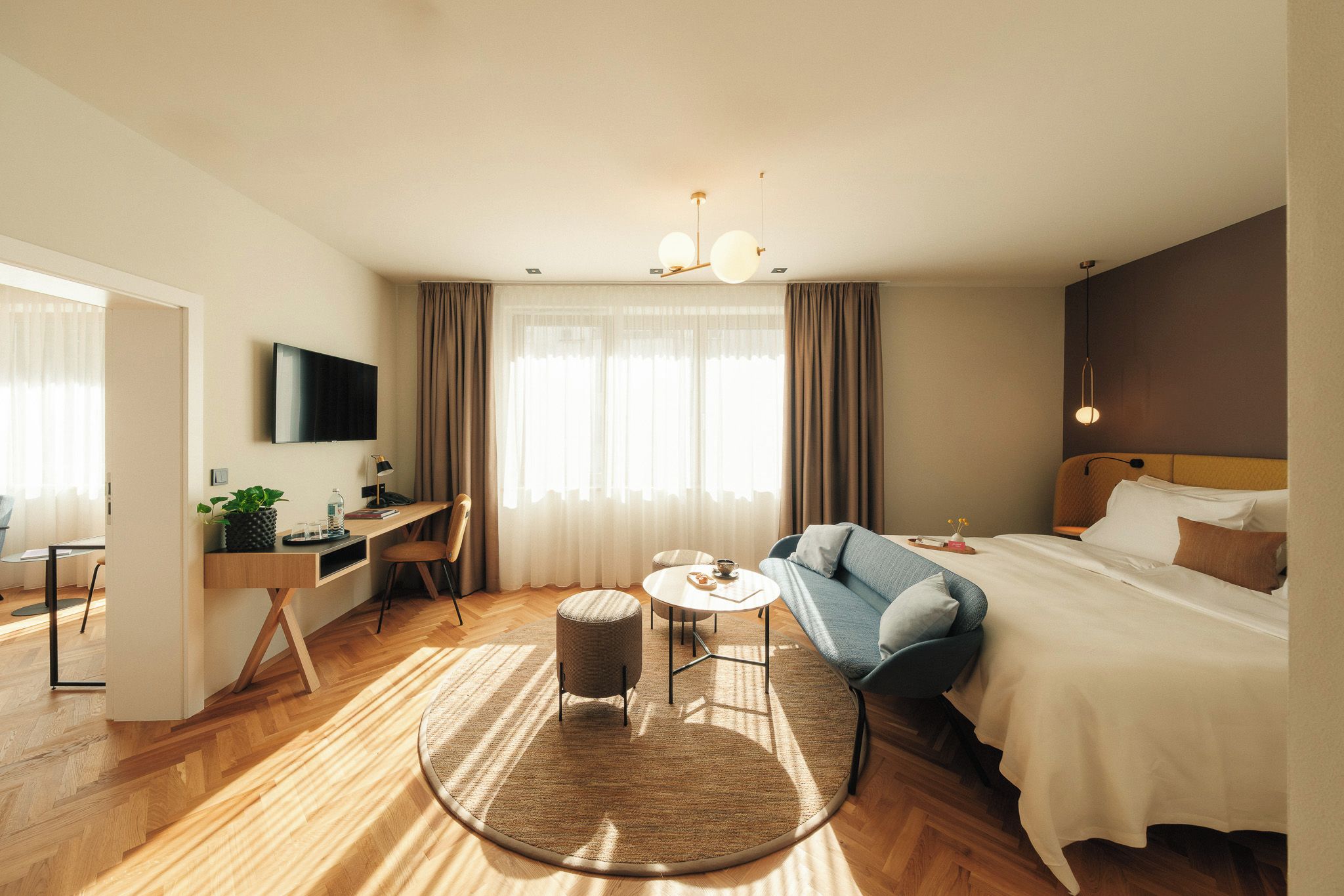 A hotel room with a bed, a desk, a chair, a TV, and a window with curtains.