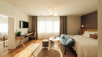 A hotel room with a bed, a desk, a chair, a TV, and a window with curtains.