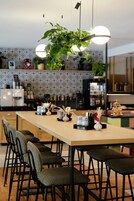 Uma cozinha moderna com uma mesa de madeira comprida, cadeiras pretas, plantas pendentes e diversos eletrodomésticos.