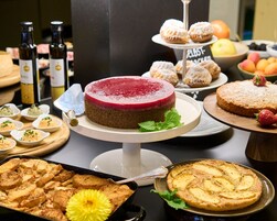 Un tavolo con dolci, tra cui torte assortite e pasticcini, come una torta red velvet, crostate di frutta e altre delizie.