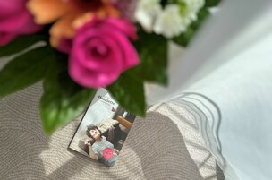 Revista sobre uma superfície texturizada, com uma vista parcial de um quarto e uma rosa rosa.