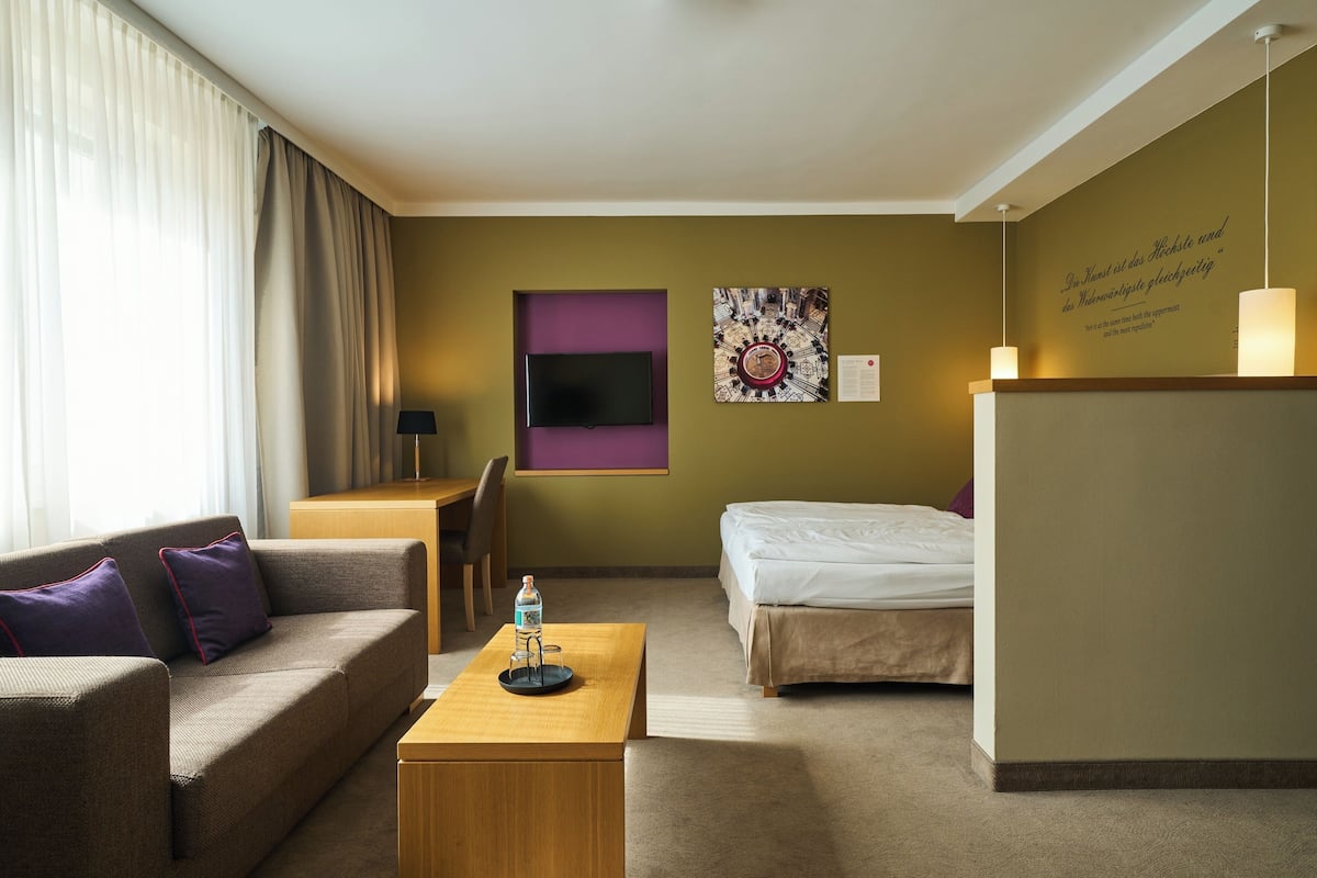 A hotel room with a sofa, a bed, a desk, and a TV.